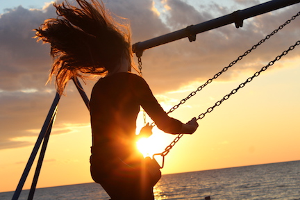 Woman on a beach swinging on a swing set. 